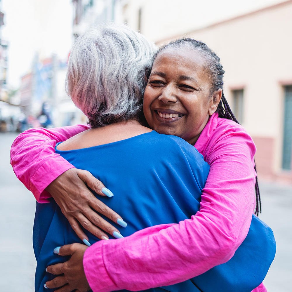 A multracial senior woman hugs a woman with her back to the camera